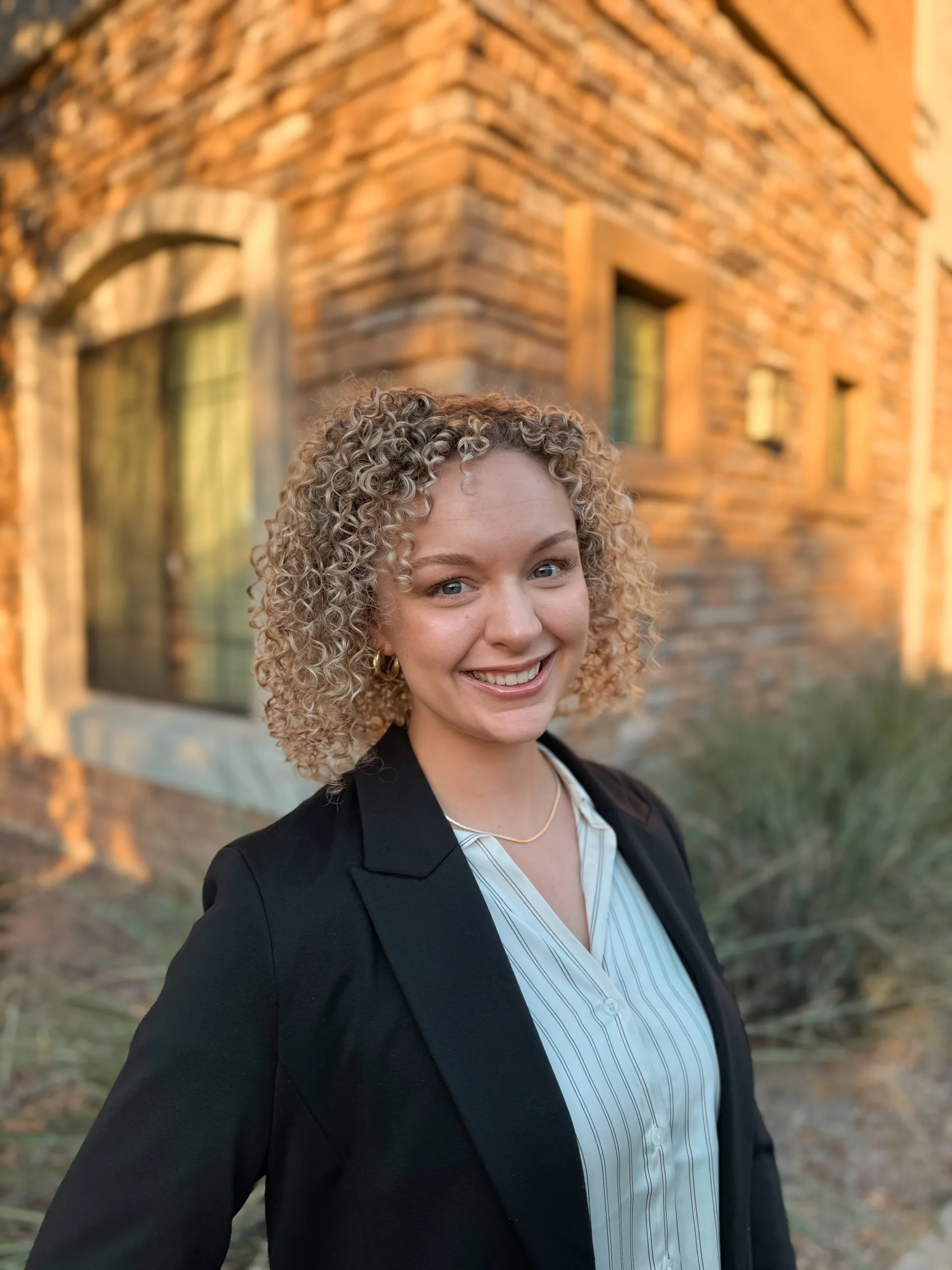 woman with light curly hair stands in front of brick building