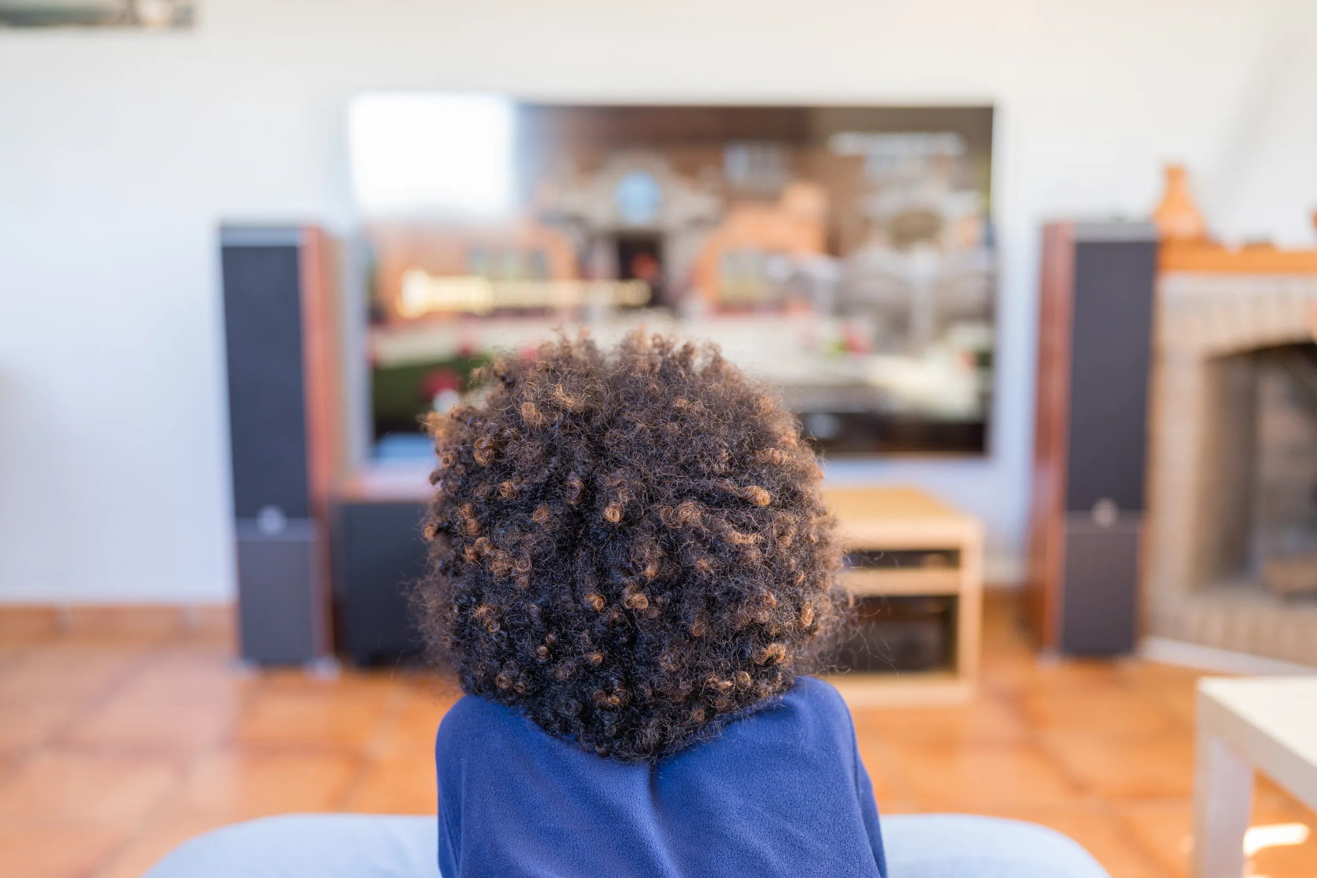 Young boy with afro hair watching the tv in the living room at home.
