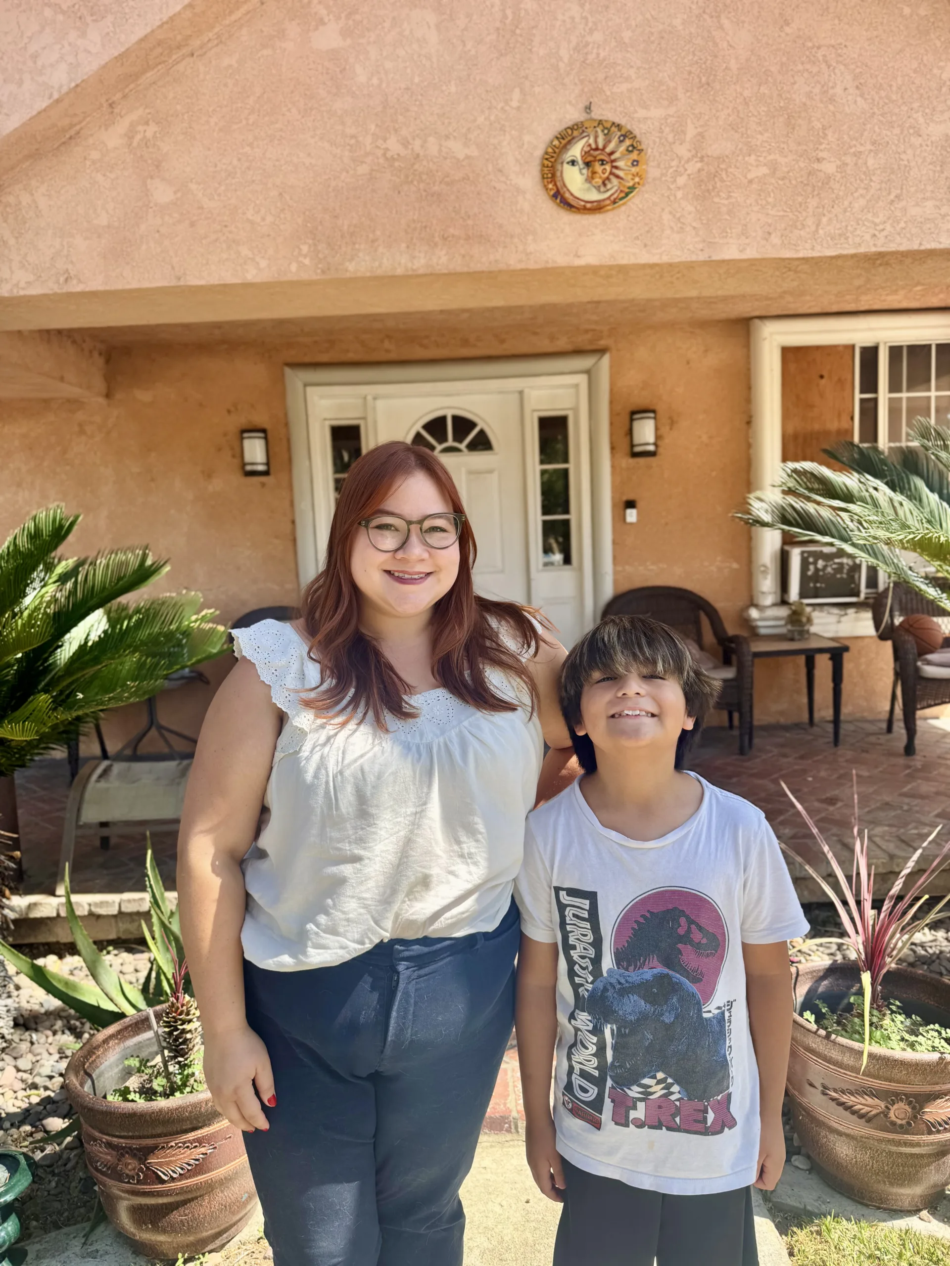 A Board Certified Behavior Analyst (BCBA) and a child stand together outdoors in front of a home during an ABA therapy session.